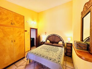 A bedroom with a bed, a wardrobe, a mirror, and a nightstand with a lamp.