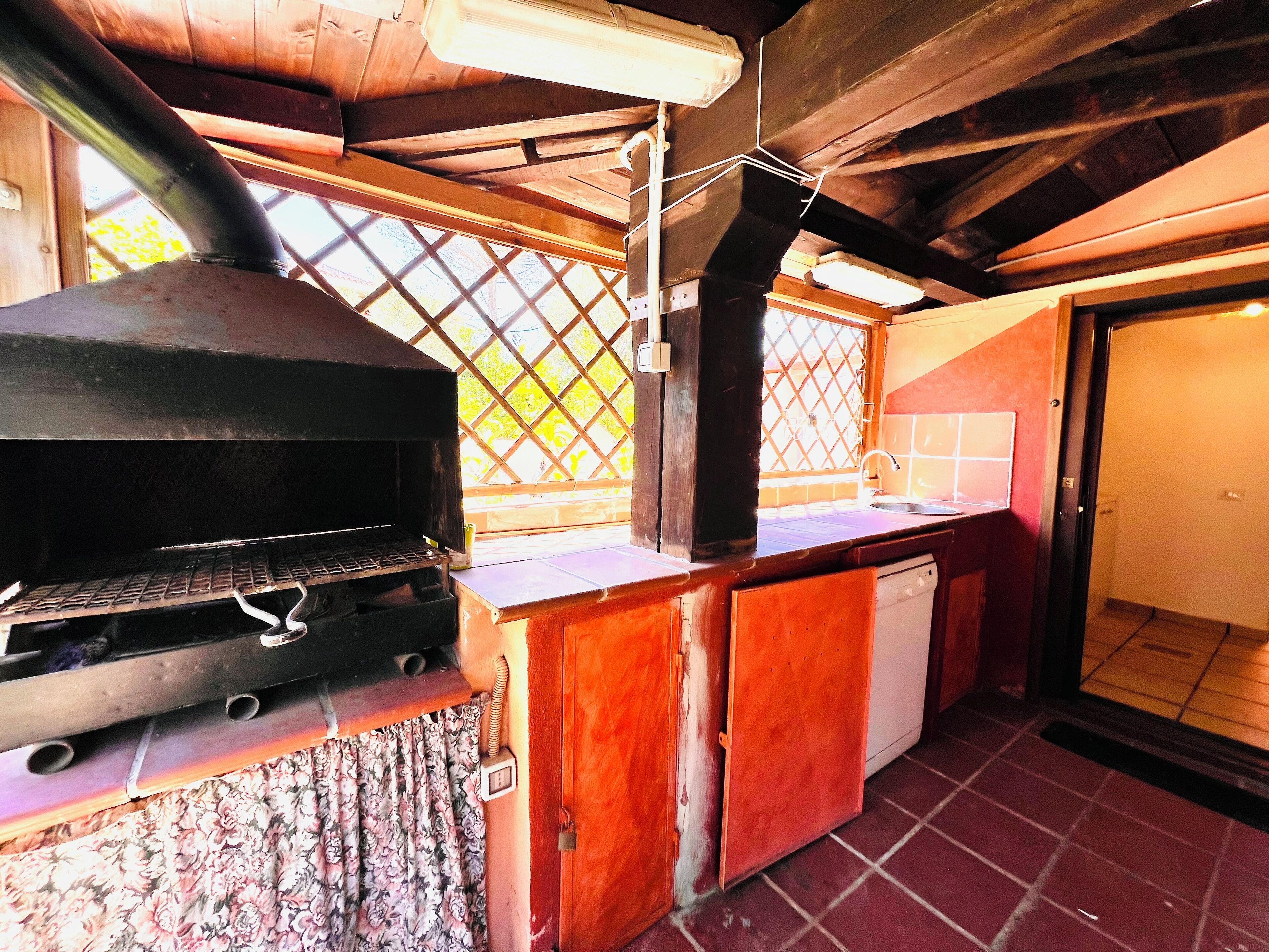 A kitchen with a built-in grill, wooden cabinets, a sink, and a window with a lattice design.