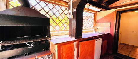 A kitchen with a built-in grill, wooden cabinets, a sink, and a window with a lattice design.