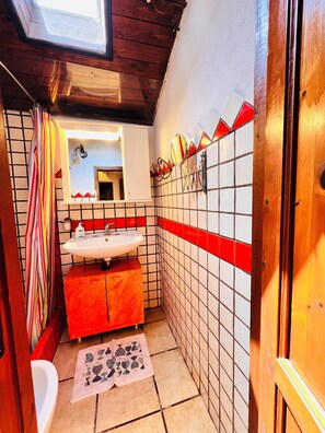 A small bathroom with a white sink, red and white tiled walls, a wooden door, and a skylight.