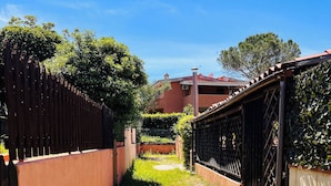 A narrow alleyway with a gravel path, flanked by a wooden fence and a metal gate, leading to a building with a red roof. - Bilocale Lu Liciu H10 in Centro (San Teodoro)