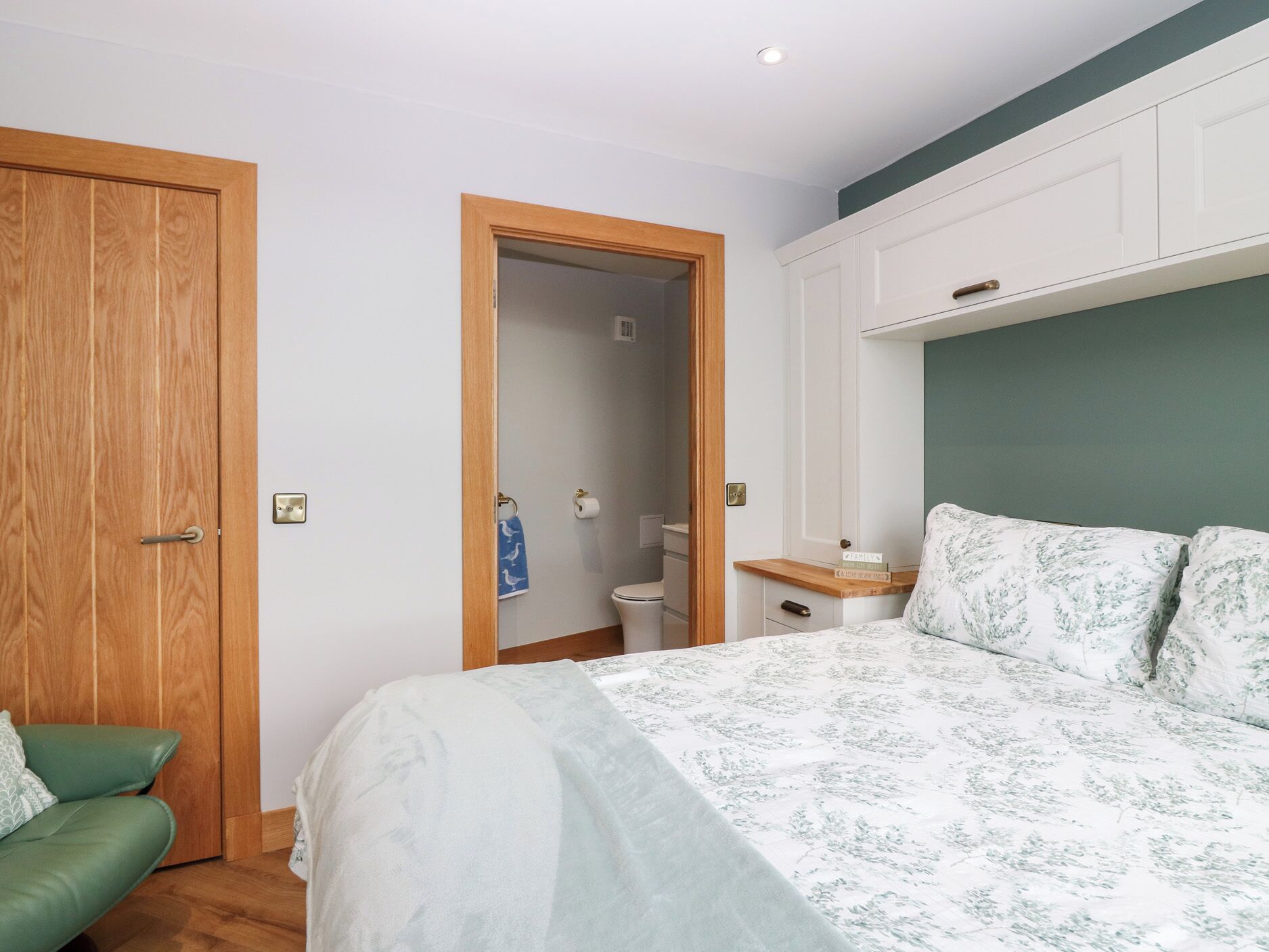 Une chambre à coucher avec un lit, un canapé vert, une armoire en bois et une salle de bain visible à travers une porte ouverte.