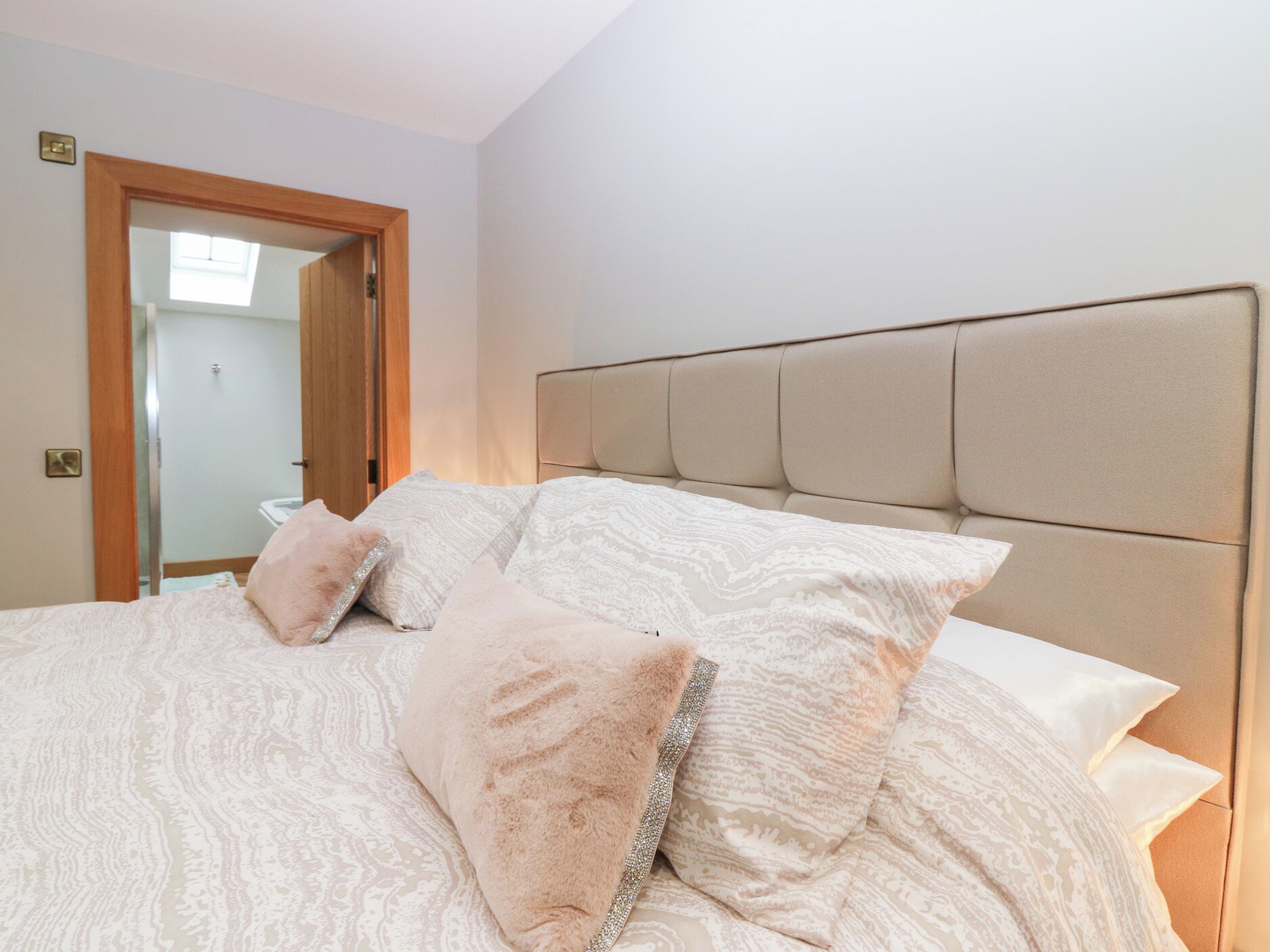 Un dormitorio con cama, cabecera y puerta que da a un baño.