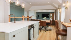 A modern kitchen with a large island, wooden flooring, and pendant lighting. - The Old Kipper Hoose (Banff)