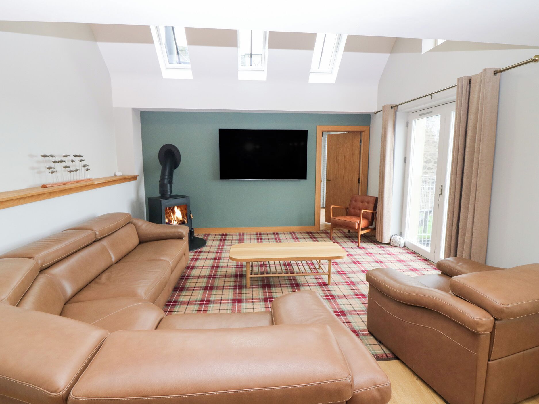 A living room with a brown leather sofa, a plaid rug, a wooden coffee table, a fireplace, and a television on the wall.