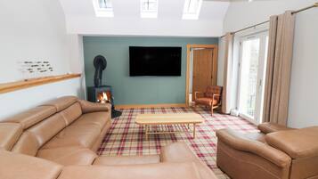 A living room with a brown leather sofa, a plaid rug, a wooden coffee table, a fireplace, and a television on the wall.
