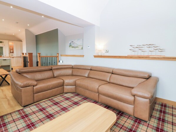 A modern living room with a brown leather sectional sofa, a plaid area rug, and a wooden dining table.