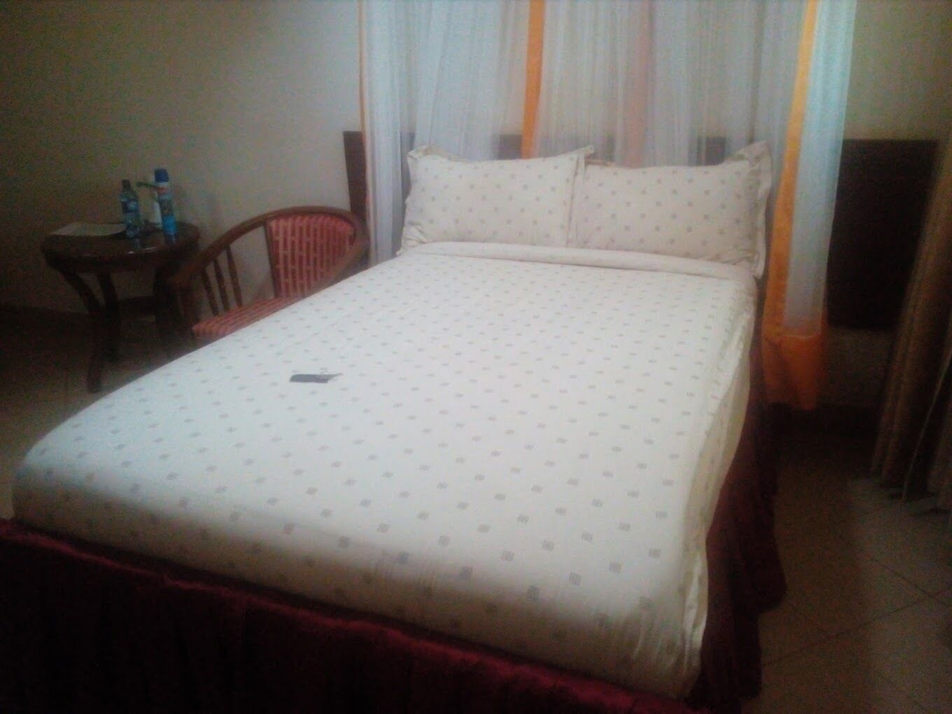 Une chambre d’hôtel standard, avec un lit, une chaise, une petite table et un rideau.