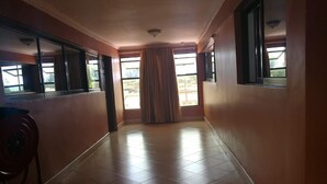 A hallway with tiled flooring, large windows with curtains, and a ceiling light fixture.