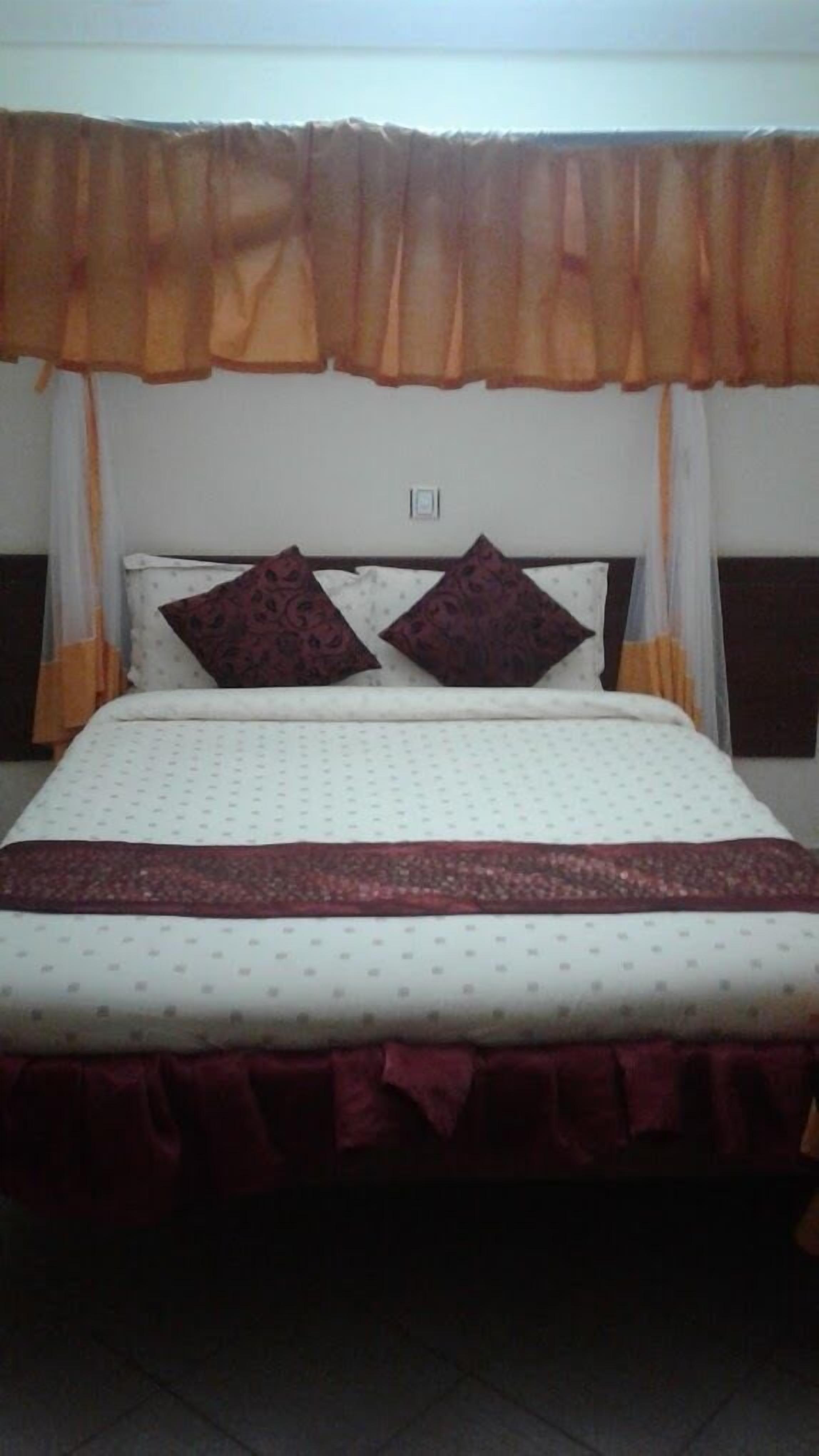 Un letto con una coperta a motivi, due cuscini e una tenda decorativa.