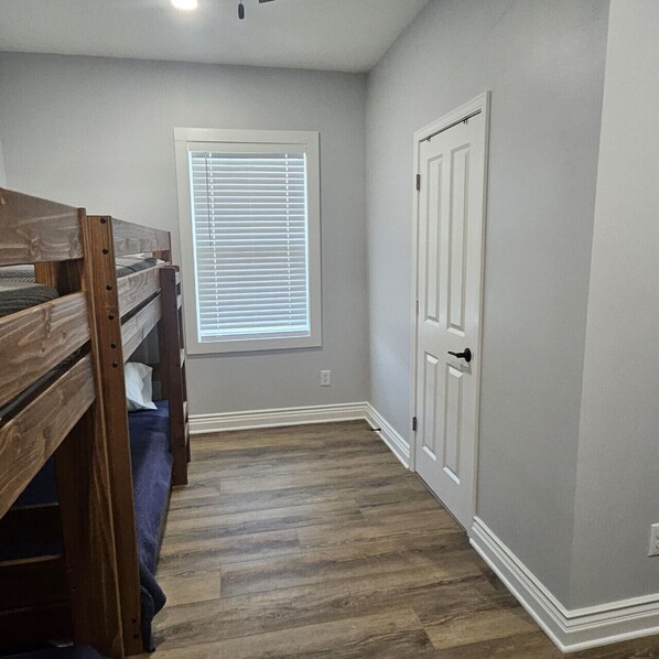 Una habitación con literas, una ventana con persianas, una puerta y suelo de madera.