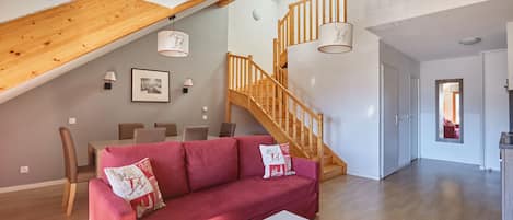 A spacious living area with a wooden staircase, a red sofa, and a dining table with chairs.