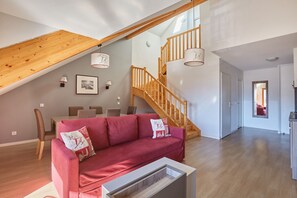 A spacious living area with a wooden staircase, a red sofa, and a dining table with chairs. - Residence Odalys Aquisana (La Salle-les-Alpes)