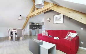 A loft-style room with a dining area, a red sofa, and a kitchen in the background.