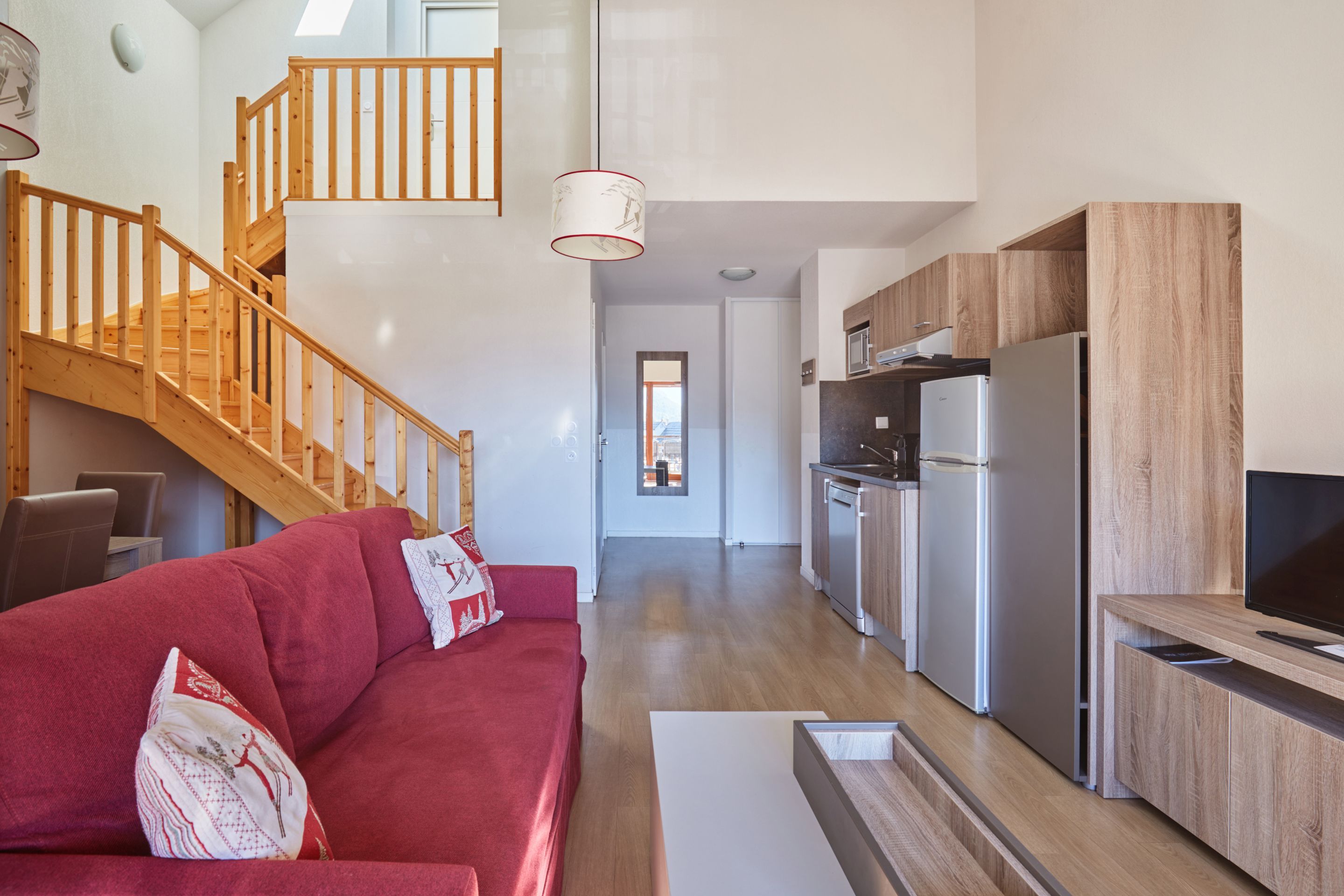 Un espacio habitable moderno con una escalera de madera, un sofá rojo, una cocina con armarios de madera y un televisor de pantalla plana.