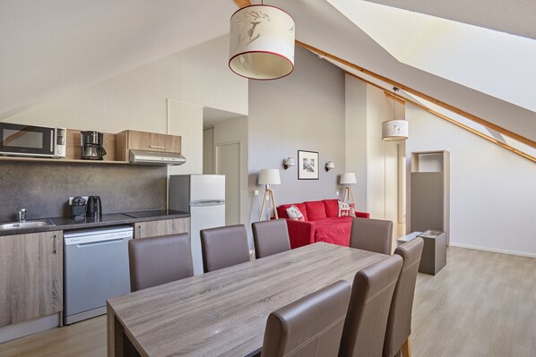A modern kitchen with a dining area, a red sofa, and a staircase.