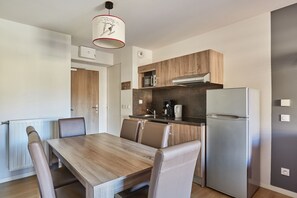 A modern kitchen with a built-in oven, microwave, and refrigerator. There is a dining table with chairs and a pendant light above it. - Residence Odalys Aquisana (La Salle-les-Alpes)