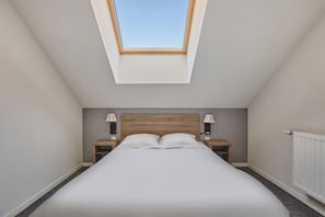 Quarto com clarabóia, uma cama, duas mesas de cabeceira e um radiador.