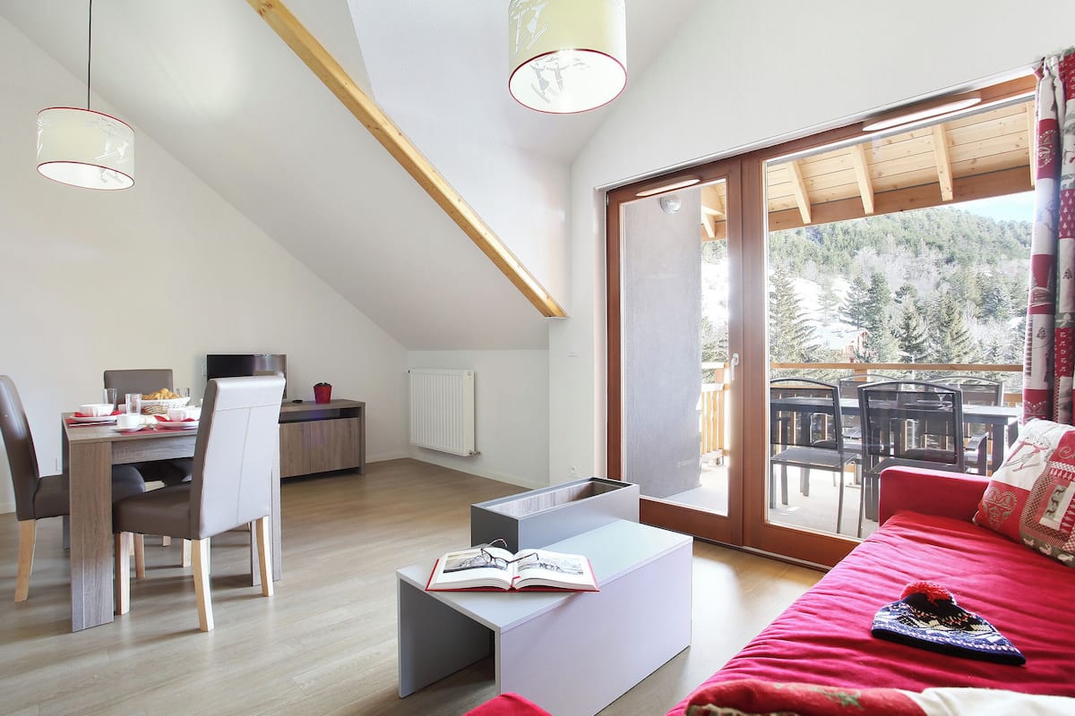 Ein modernes Zimmer mit Essbereich, einem Bett und einem großen Fenster mit Blick auf Bäume.