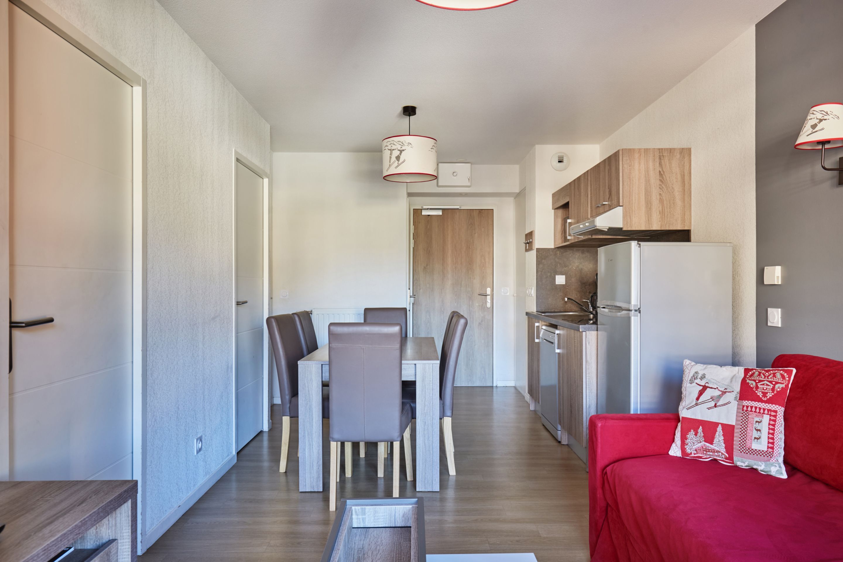 Cozinha moderna com forno embutido, área de jantar com mesa e cadeiras, e um sofá vermelho com almofada decorativa.