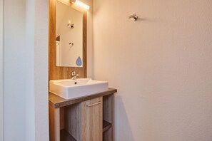 A bathroom with a white sink, wooden vanity, and a mirror with a light above it. - Residence Odalys Aquisana (La Salle-les-Alpes)