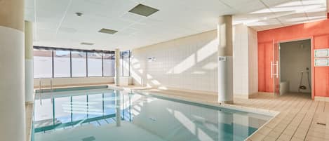 Una piscina con agua cristalina, rodeada de paredes con azulejos e iluminación empotrada en el techo.