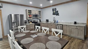 Een moderne keuken met een centraal eiland, houten kasten en een eethoek met een donker houten tafel en witte stoelen.
