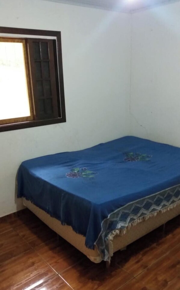 Een kleine kamer met een bed, een raam met houten kader en een houten vloer.