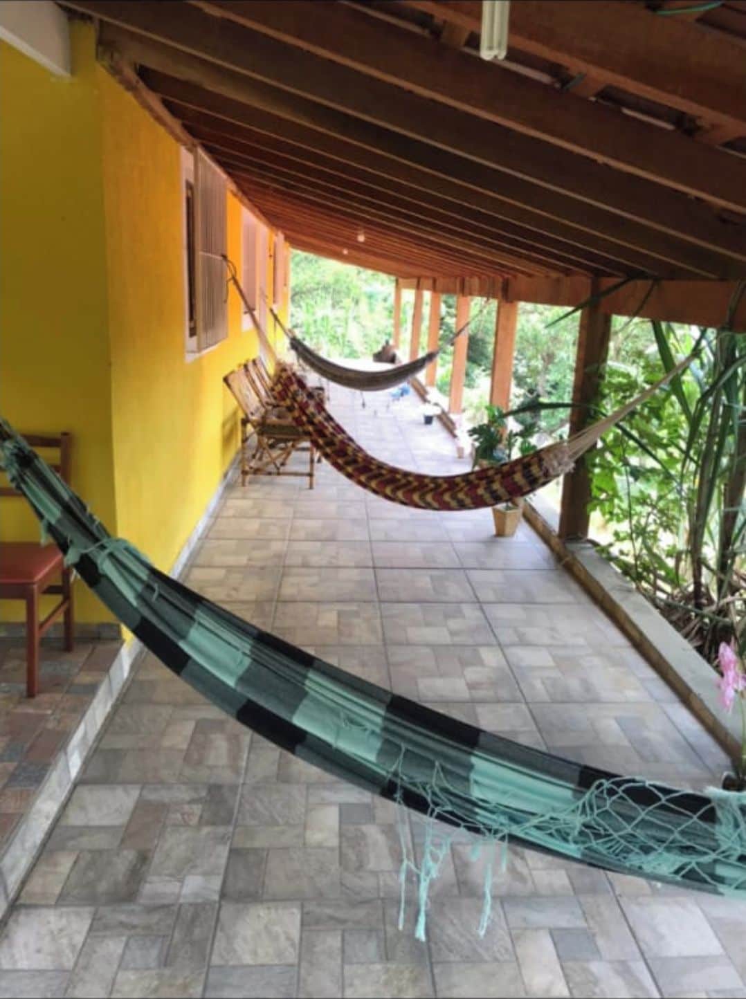 A hammock under a wooden pergola, a tiled patio, and a yellow wall.