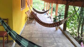 A hammock under a wooden pergola, a tiled patio, and a yellow wall.