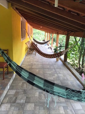 Una hamaca bajo una pérgola de madera, un patio con baldosas y una pared amarilla.