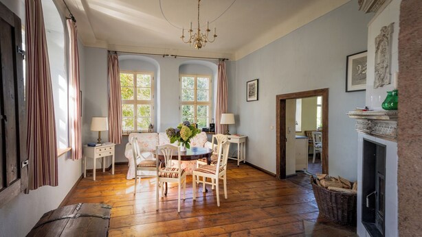 A spacious room with wooden flooring, a dining table with chairs, a sofa, and a fireplace.