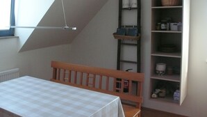 A room with a checkered table, a wooden bench, a slanted ceiling, a ladder, and shelves with various items.