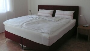 A bed with white bedding, a wooden headboard, and a bedside table with a lamp.