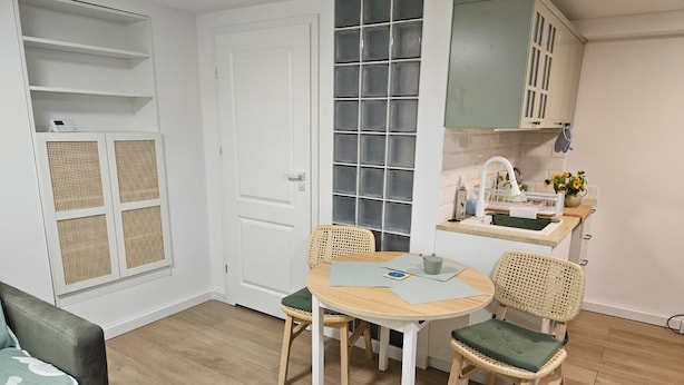 A compact living space with a dining table, two chairs, a sofa, a kitchenette, and a door with a window.