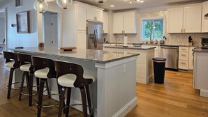 Una cucina moderna con isola centrale, sgabelli da bar, elettrodomestici in acciaio inossidabile e illuminazione a sospensione.