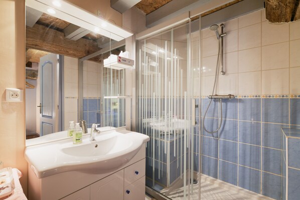 A bathroom with a glass shower enclosure, a sink with a mirror, and tiled walls.
