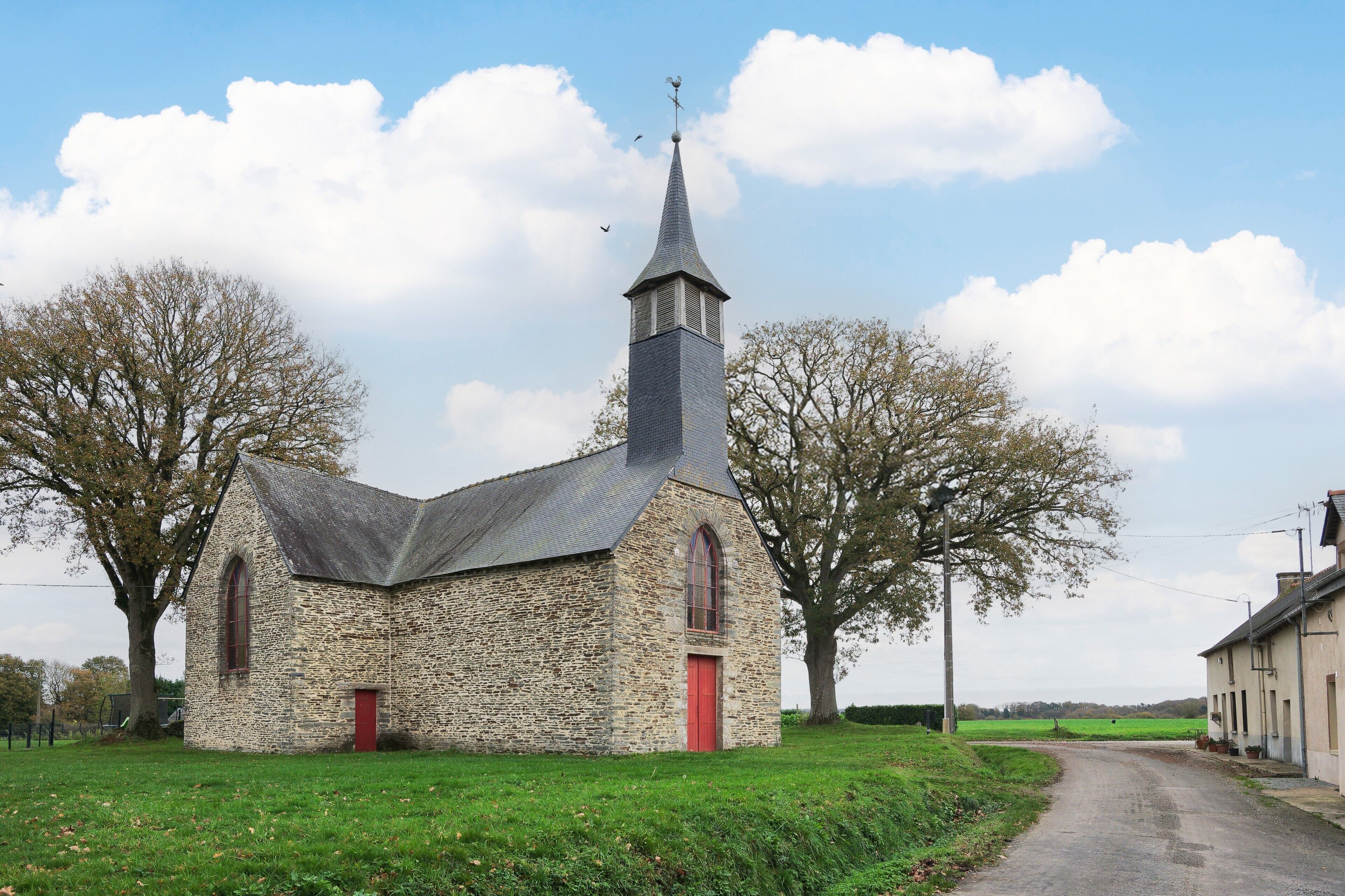 Une église en pierre avec une porte rouge et un clocher élevé.