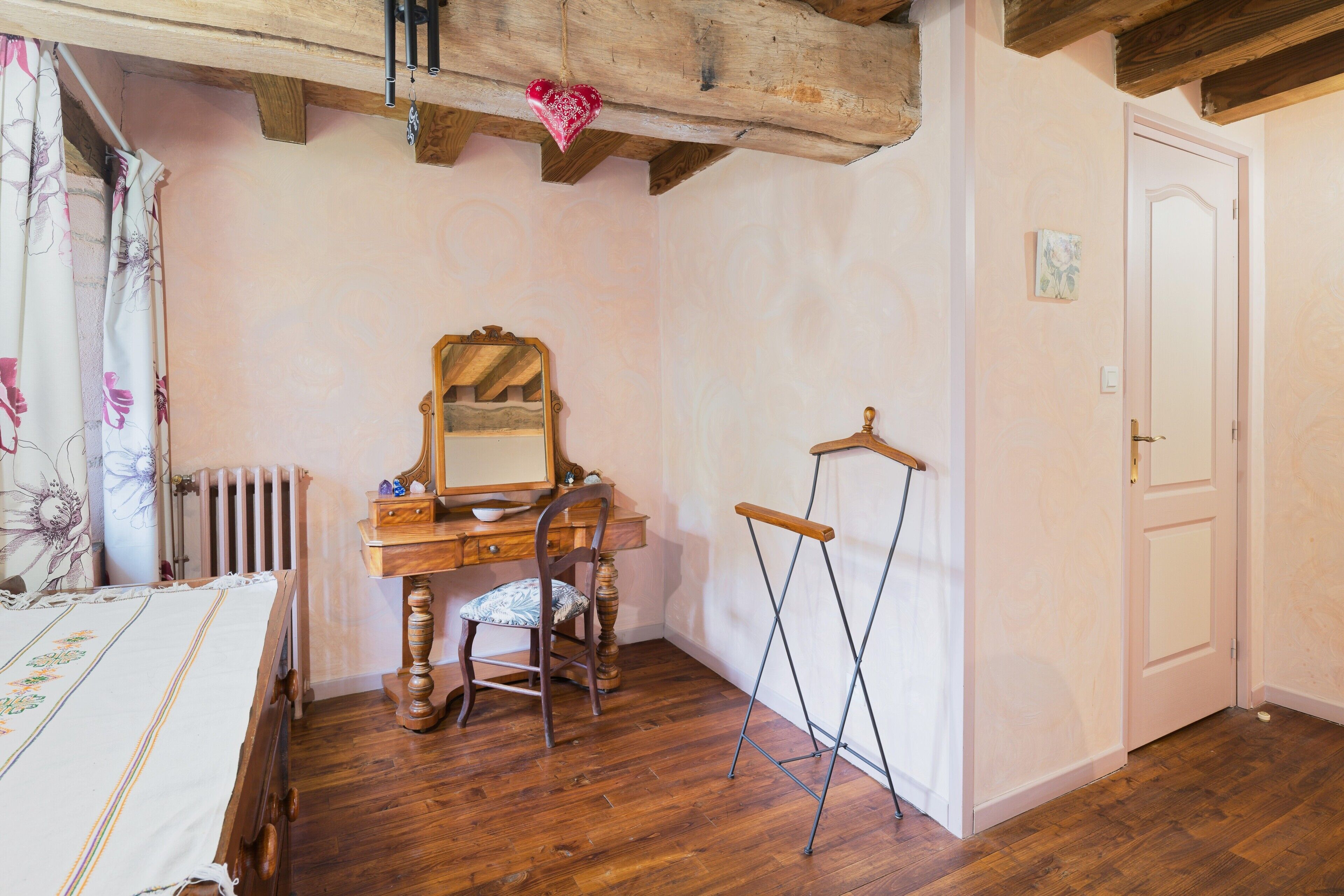 Ein Schlafzimmer mit einem Holzbett, einem Schminktisch, einem Sessel, einem Spiegel, einer Heizung und einer Tür.