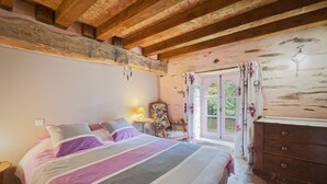 Un dormitorio con cama, vigas de madera en el techo, un aparador y una ventana con cortinas.