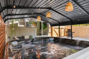 A hot tub area with a brick wall, wooden deck, and hanging pendant lights. - Spacious Uptown Retreat w/ Jacuzzi (Charlotte)