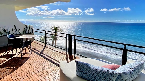 Ein Balkon mit Blick auf den Ozean, ein Tisch mit Stühlen und eine Couch mit Kissen.