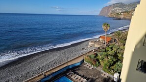 Blick auf die Küste mit einem Kiesstrand, einem Schwimmbad und einem Gebäude mit einem Balkon mit Meerblick.