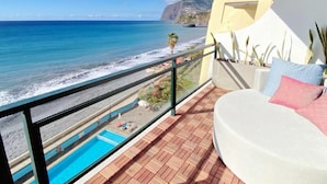 Ein Balkon mit Blick auf den Ozean, ein Pool und ein weißes Sofa mit Kissen.
