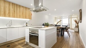 Eine moderne Küche mit weißen Schränken, einer zentralen Kochinsel mit Backofen und einem Essbereich mit Tisch und Stühlen.