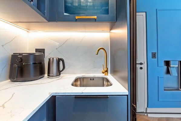 A modern kitchen with a built-in coffee maker, a kettle, and a sink with a gold faucet.