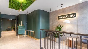 A modern reception area with a green wall, a sign reading "The Valour," and a staircase with a metal railing. - The Valour 702 (Cape Town)