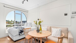 A modern bedroom with a large window, a bed, a sofa, a round table, and a vase with flowers. - The Valour 702 (Cape Town)