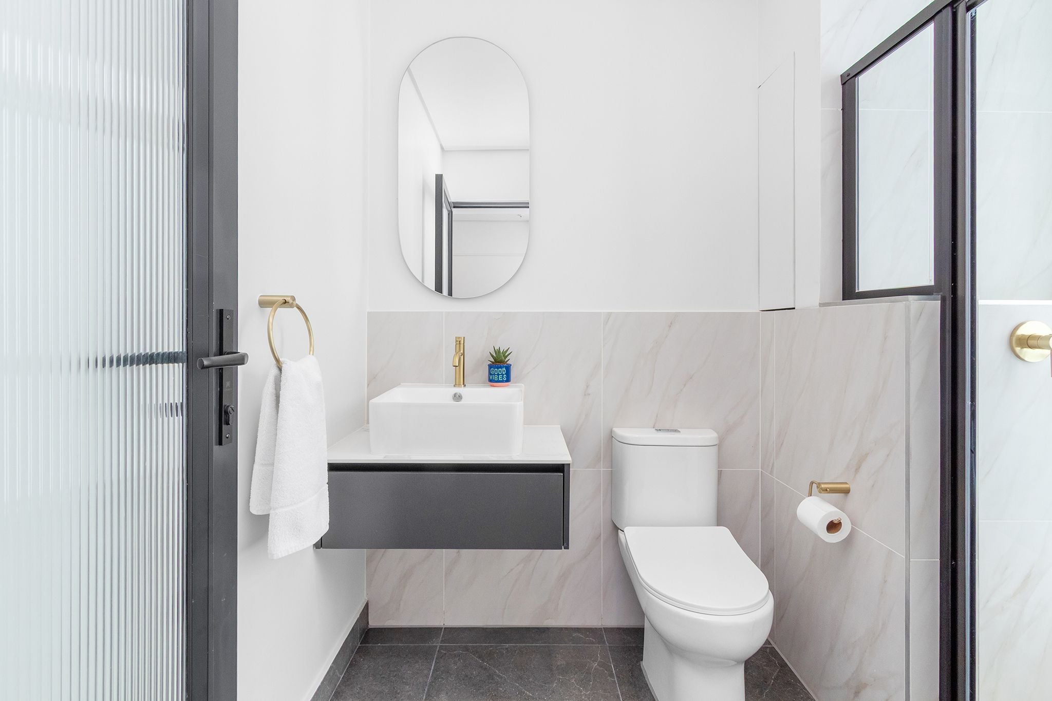 Une salle de bain moderne avec un lavabo blanc, des toilettes et un miroir.