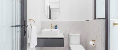 Une salle de bain moderne avec un lavabo blanc, des toilettes et un miroir.